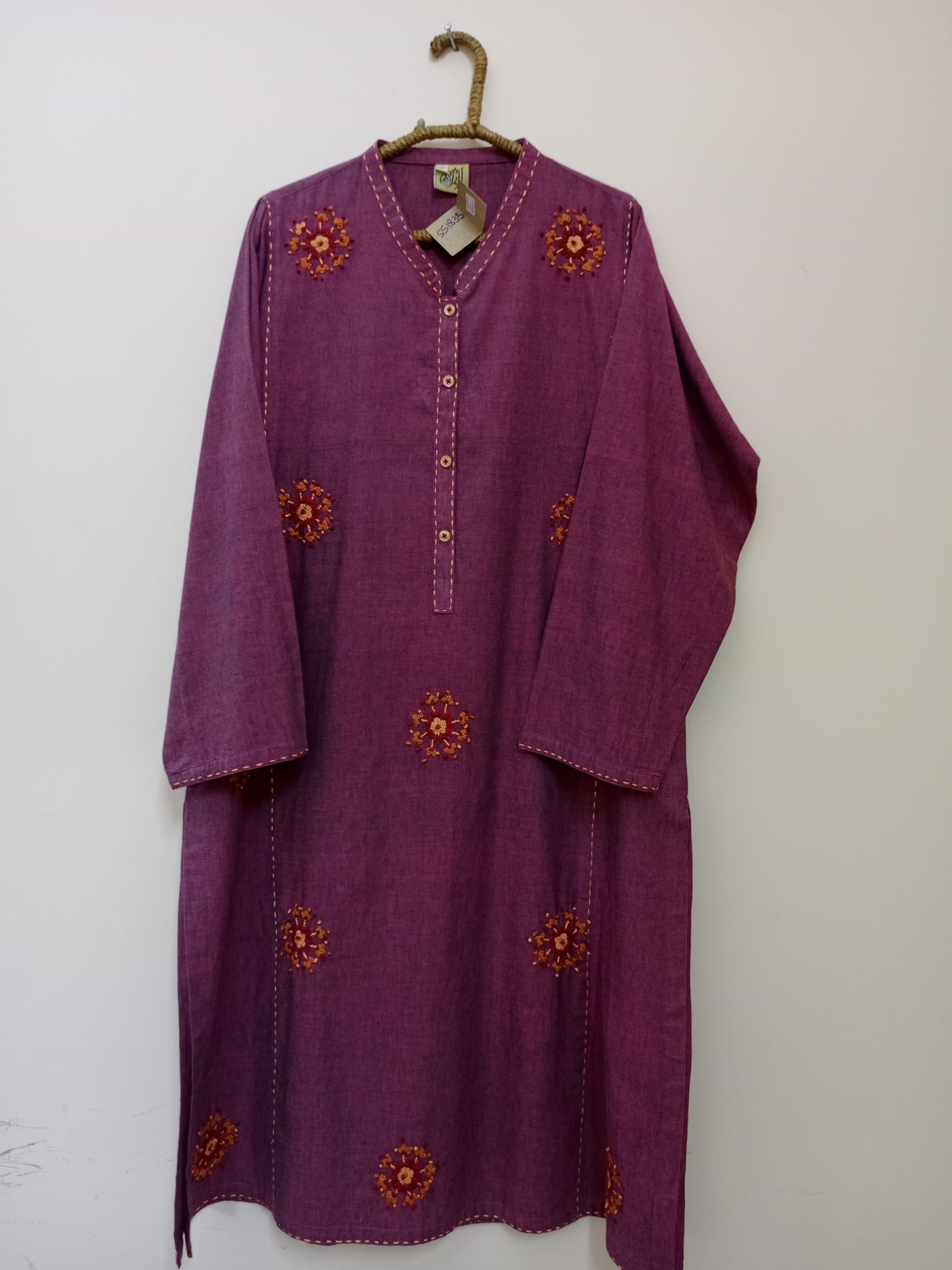 A graceful shirt featuring intricate floral hand embroidery on a rich magenta base. Perfect for elegant everyday wear with a unique buttoned neckline and spaced floral motifs.
